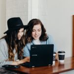 two woman sitting near table using Samsung laptop