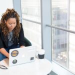 woman sits on padded chair while using MacBook during daytime