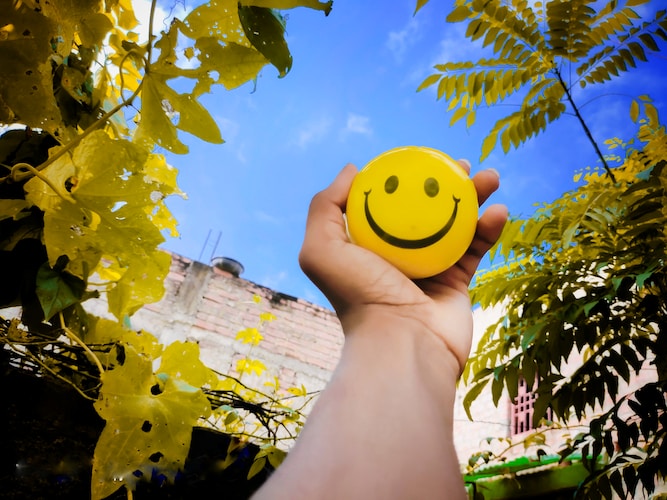 a hand holding a yellow smiley face ball