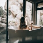 woman in white bathtub holding clear drinking glass